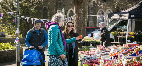 A group of people at a market stall full of fresh fruit and veg. 