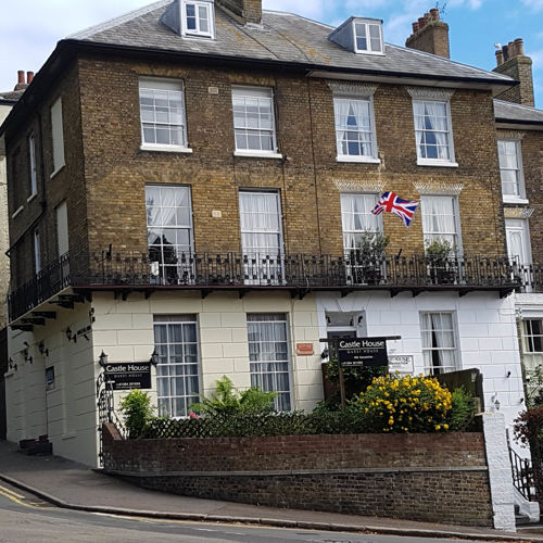 A large, period brick building with a wrought iron balustrade and period windows on a corner.