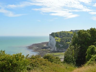 A green-blue sea, glimpse of beach and edge of white cliffs and green landscape in the foreground.