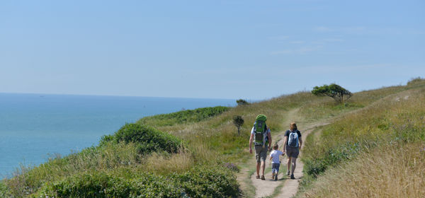 Two adults holding hands with a small child walking on the White Cliffs of Dover - blue sea and sky.