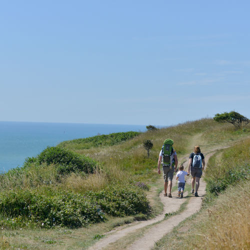 Two adults holding hands with a small child walking on the White Cliffs of Dover - blue sea and sky.