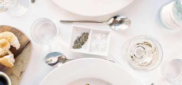 A meal for two laid on a white table cloth viewed from above. 