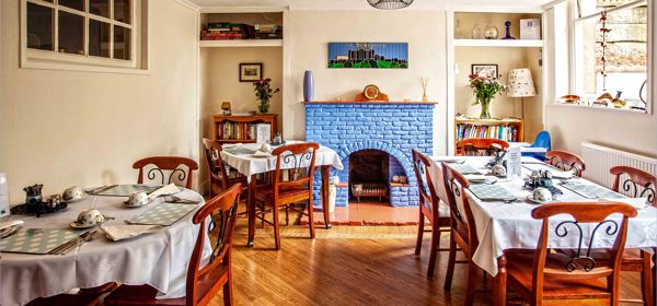 A dining room with three tables and chairs laid with tablecloths and crockery for breakfast.