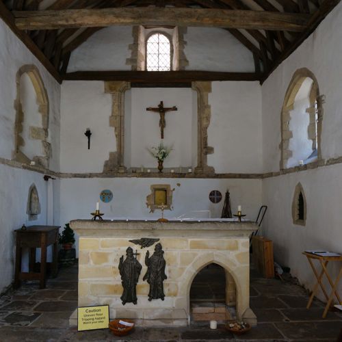 The interior of St Edmunds Chapel with a rough stone floor, whitewashed walls and a central stone alter.