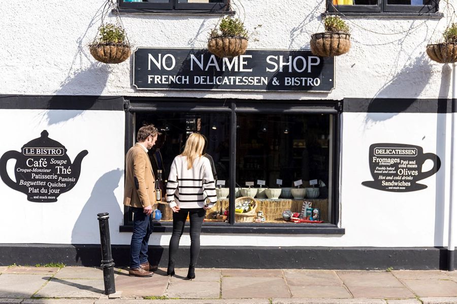 The exterior of the No Name Shop in Sandwich with a couple looking in the window displaying bowls of olives.