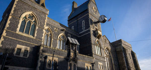 An imposing flint-faced building with arched windows and other detailing.