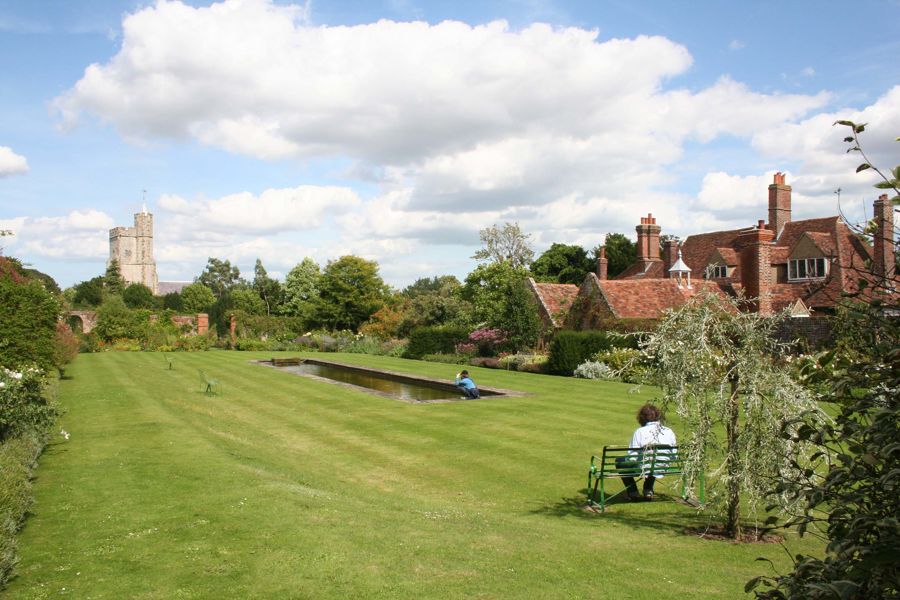 A green lawn with a long rectangular pond, a person sitting on a bench.