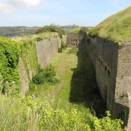 Exterior image of the Drop Redoubt fortress, brick walls and a green grass-lined dry moat. 