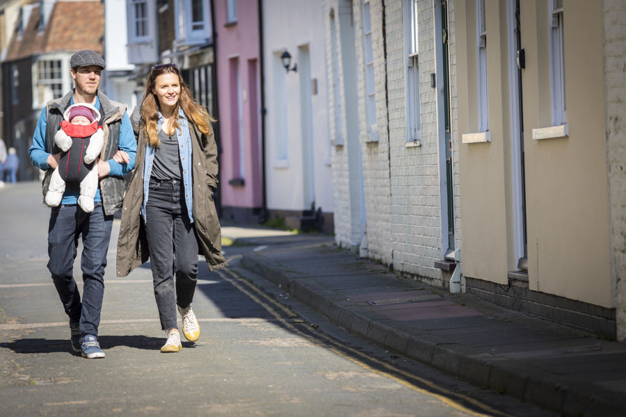 A couple walking arm in arm - the man has a baby in a sling strapped to his chest - through the colourful streets of Deal's conservation area.