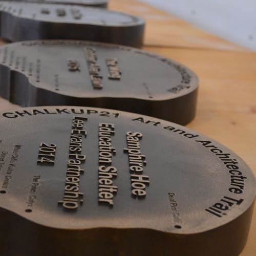 A series of brown metallic raised plaques set into wood detailing stops on the CHALKUP21 Art and Architecture Trail 