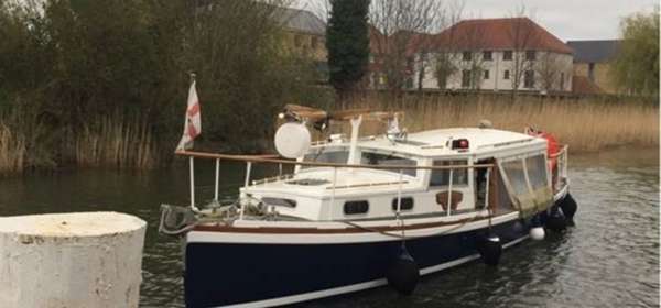 A wooden boat with a navy blue hull and white deck on the River Stour with reedbeds in the background.