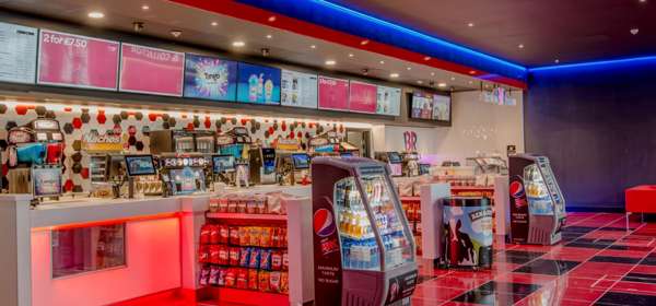 Interior of cinema reception with food and drink displays and shiny red-and-white tiled floor.