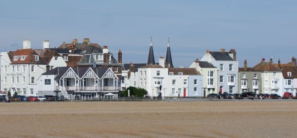 A row of white and pastel coloured buildings with a shingle beach and sea in the foreground.