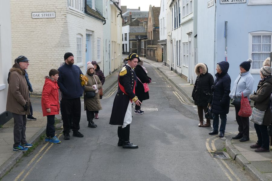 A man dressed in Napoleonic costume talking to a group of tourists in the winding streets of Deal.
