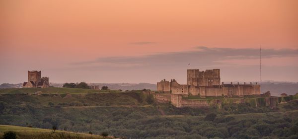 Dover Castle from a distance in the early morning light with a pink sky and greenery in the foreground.