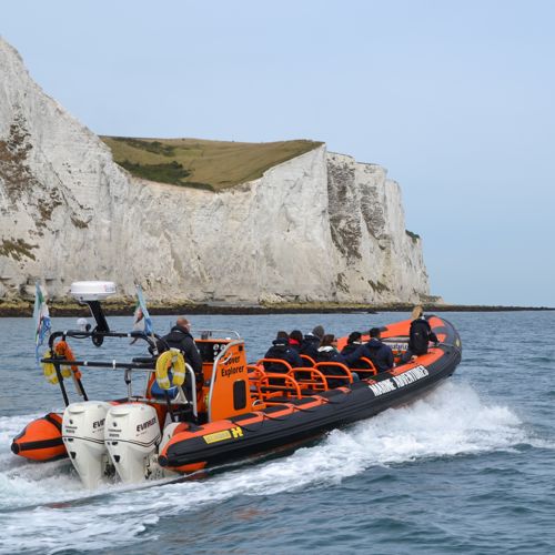 People aboard a black and orange Dover Sea Safari RHIB heading past the White Cliffs on a blue sea with blue sky overhead.