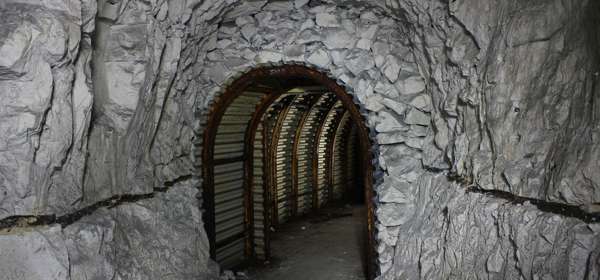 An arched tunnel entrance hewn out chalk and lined with corrugated metal and iron arches.