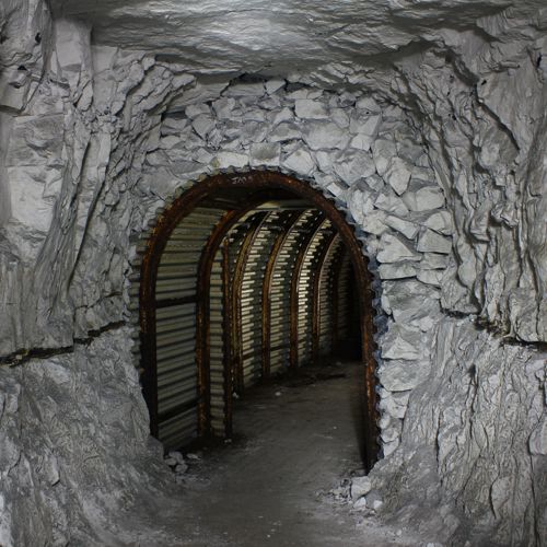 An arched tunnel entrance hewn out chalk and lined with corrugated metal and iron arches.