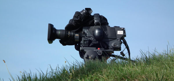 Film camera sitting on grass with blue sky behind.