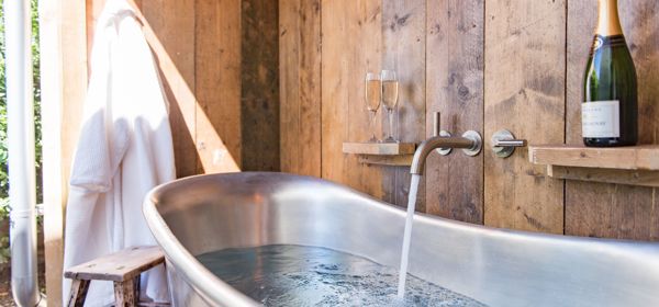 A metal bathtub filling up with water in a wood-panelled room.