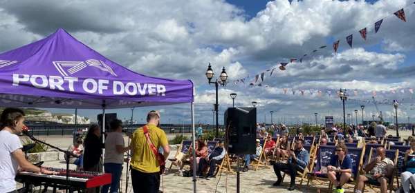 A crowd of people in deckchairs and a band playing under a gazebo on Dover Marina Curve.