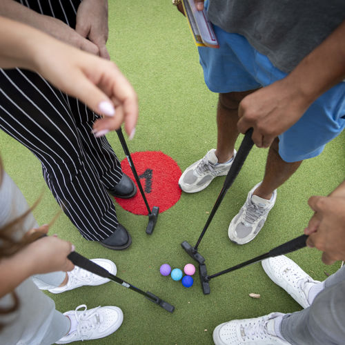 Looking down at four golf balls and clubs and four pairs of feet standing in a circle.