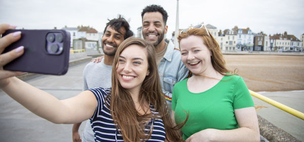 A group of four young people taking a selfie on Deal Pier with the town and seafront in the background