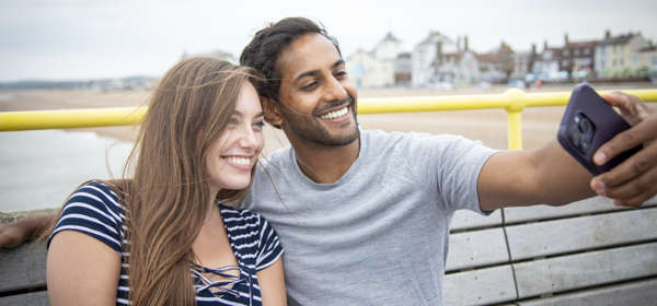 A woman wearing a striped t-shirt and a man wearing a grey t-shirt smiling taking a selfie