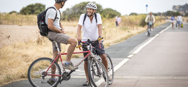 Two people on bikes chatting on a cycle path with others in the background.