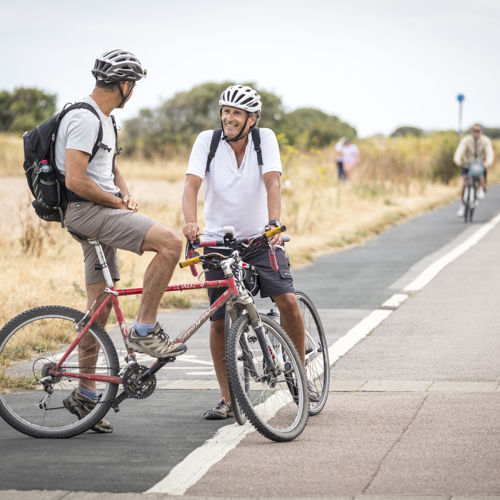 Two people on bikes chatting on a cycle path with others in the background.