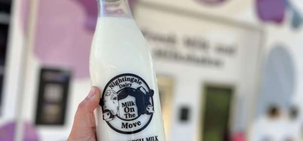 A full milk bottle being held up in front of a mobile vending machine.