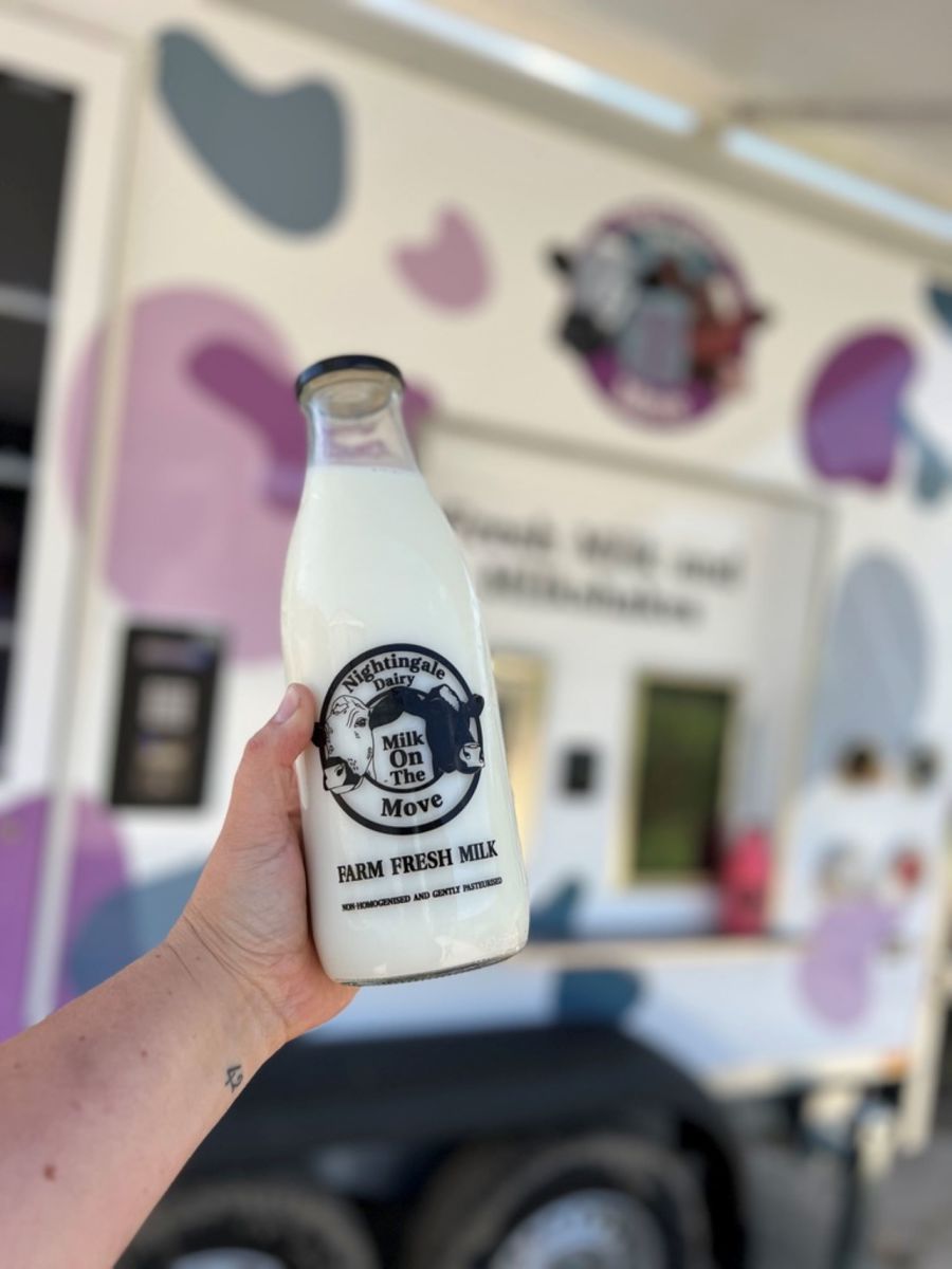 A full milk bottle being held up in front of a mobile vending machine.