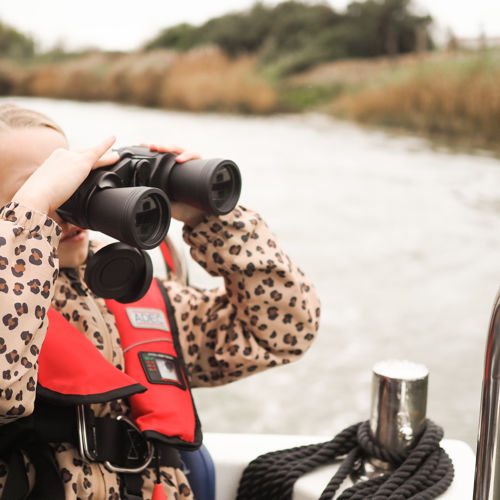 A girl looking through binoculars aboard a boat on the River Stour