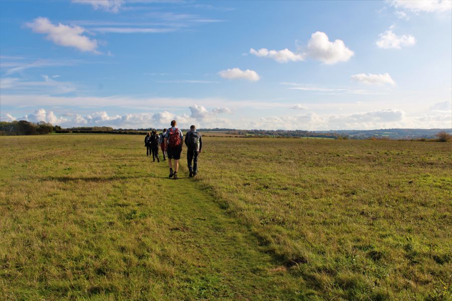 A group of walkers crossing a green grass field with far-reaching views across the countryside.