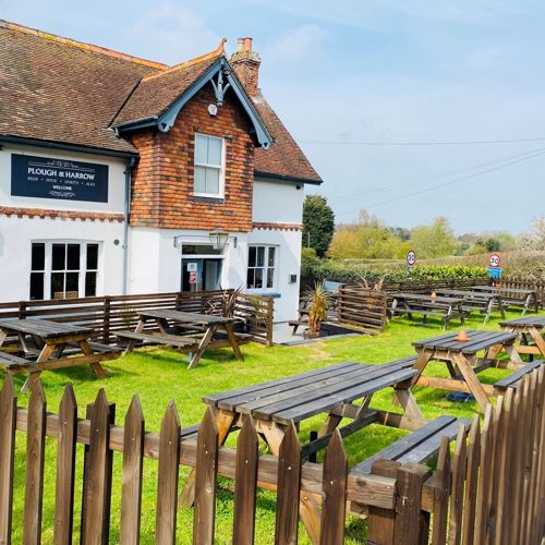 Exterior of The Plough & Harrow with tables and benches in the beer garden at the front of the pub