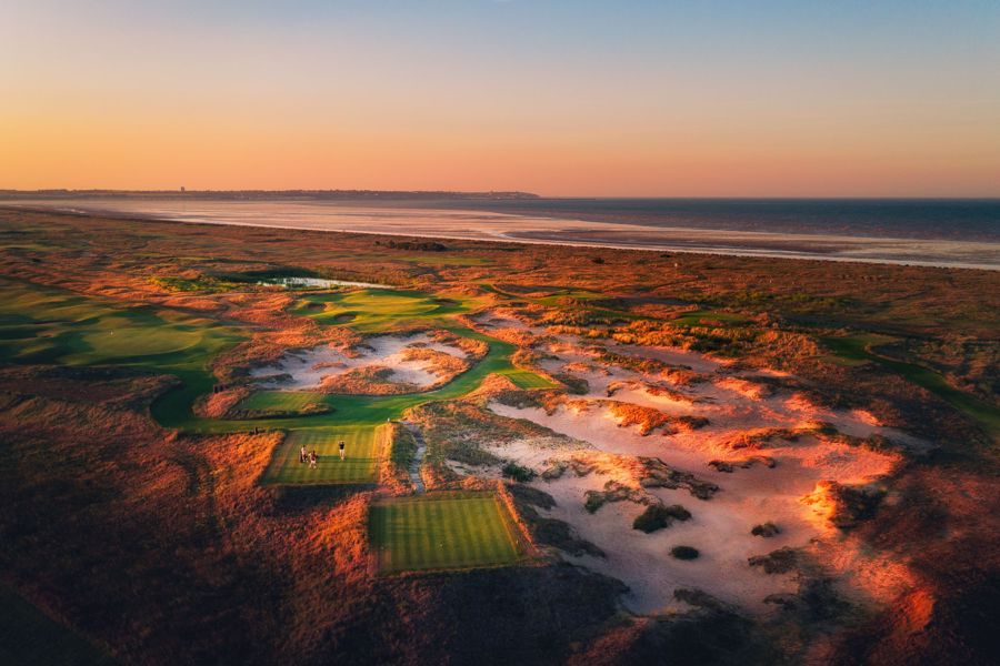 An aerial view of a series of greens and dunes with the expanse of Sandwich Bay beach and sea in the background.