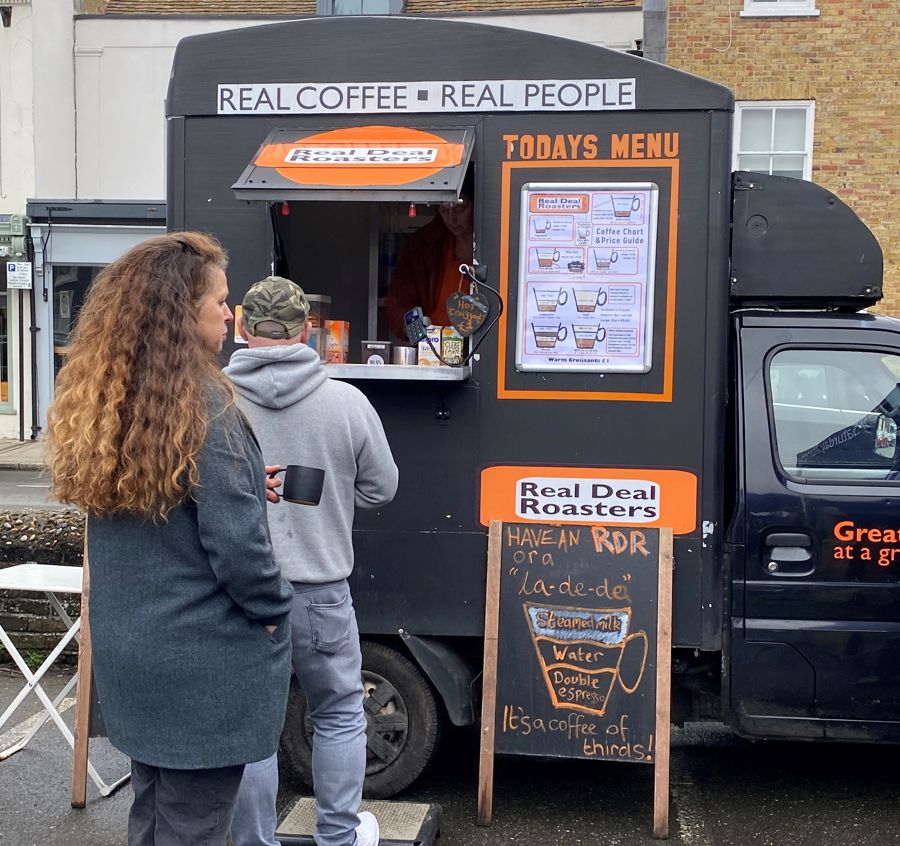 Two people queuing at Real Deal Roasters, black and orange coffee van 