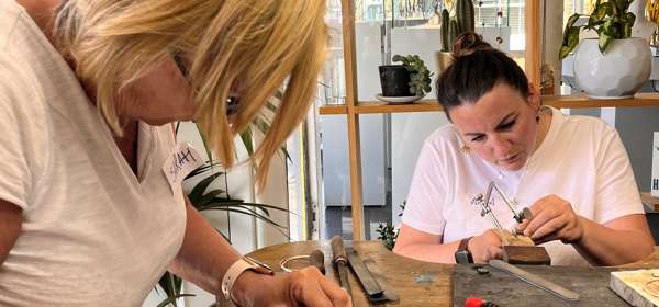 Two women at a work bench using hand tools to make jewellery.