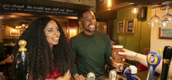 A coupe at a pub bar being handed a drink.