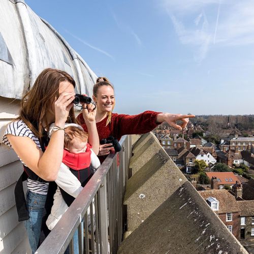 Two women, one with a baby in a papoose, at the top of St Peter's Church tower looking out over Sandwich rooftops.