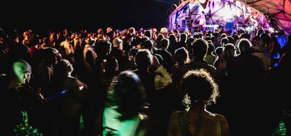 A crowd in front of an outdoor stage lit up at night.