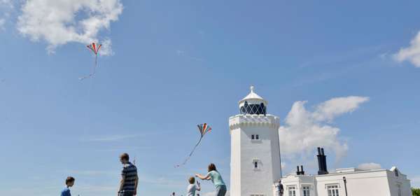 A family flying kites in front of a whitewashed lighthouse