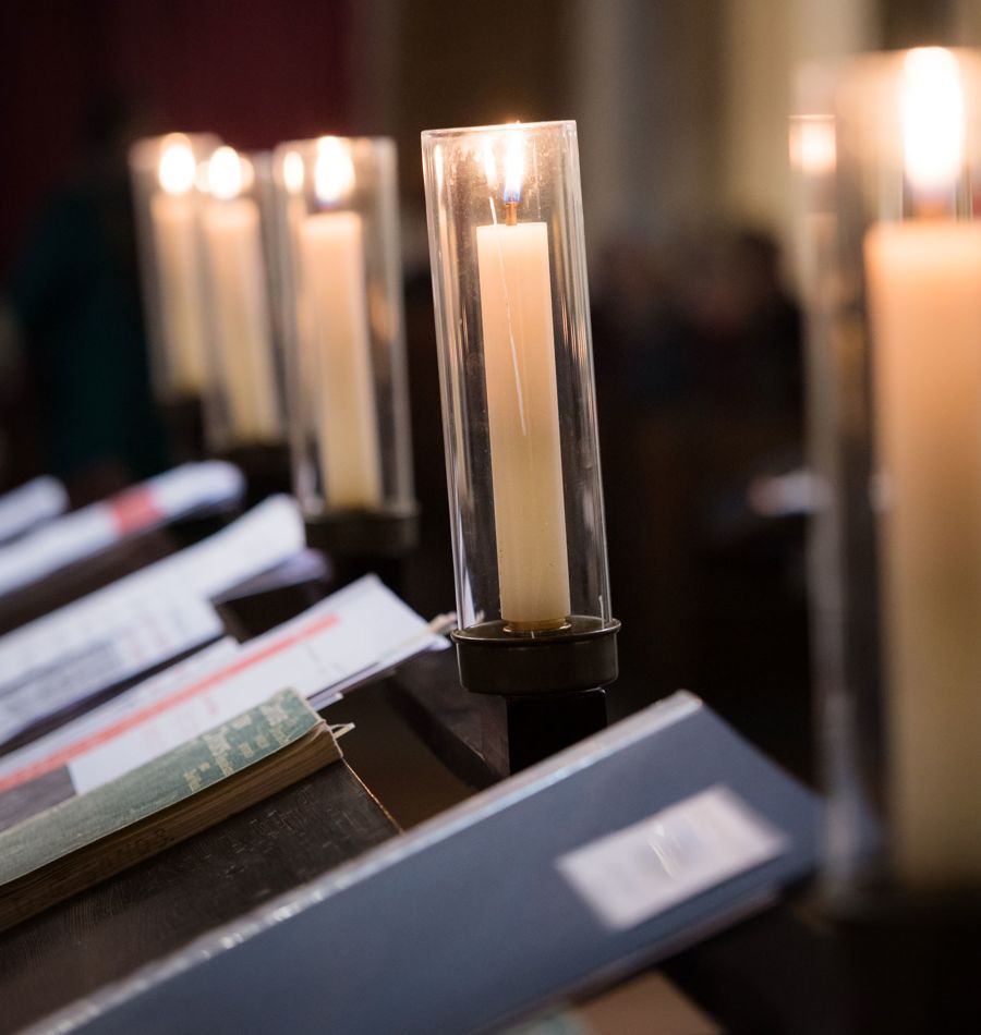 A row of candles in glass covers and hymn books on a stand.