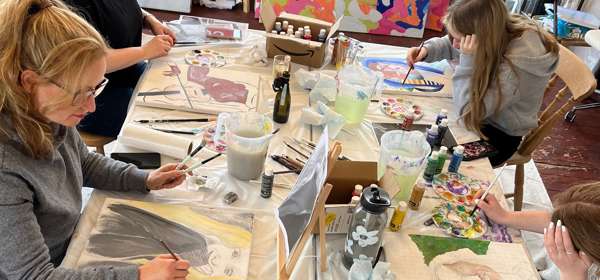 A group of four people sat at a table painting with artworks around the walls.