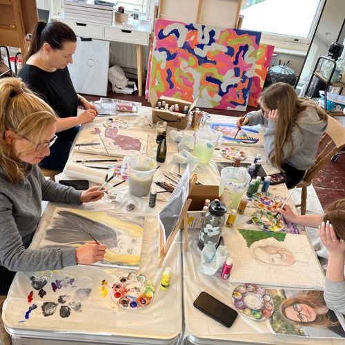 A group of four people sat at a table painting with artworks around the walls.