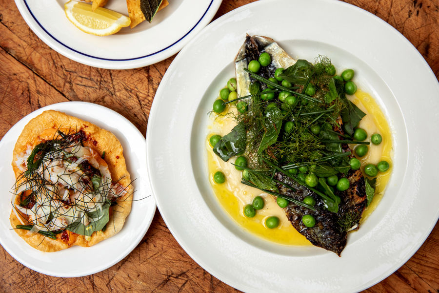 Three white plates of food, one with fish, peas and herbs, another with flatbread and toppings, another with lemons.