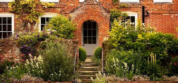 Front of Updown Farmhouse with mature garden, flower boarders and steps leading up to the front door.