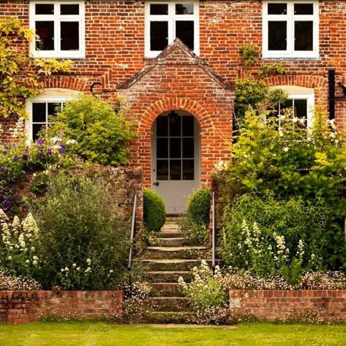 Front of Updown Farmhouse with mature garden, flower boarders and steps leading up to the front door.