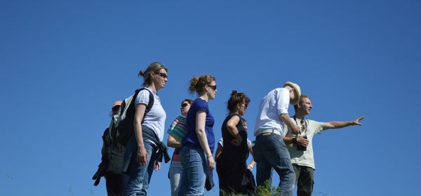 A group of people outdoors all looking in the direction the group leader is pointing. 