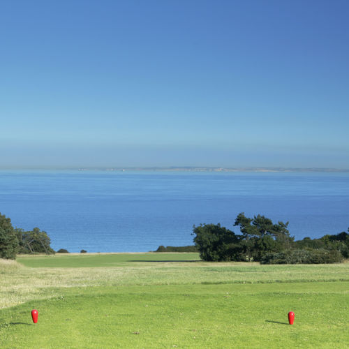 A golf green with a blue sky and sea views in the distance.